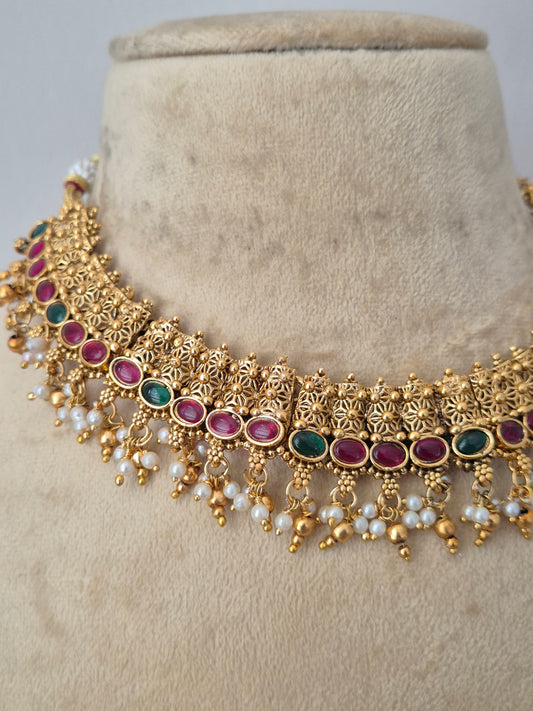 Gold filigree choker necklace with red and green stone accents and white pearl drops, a row of red and green gemstones, and a fringe of hanging white faux pearls, by naitri.in
