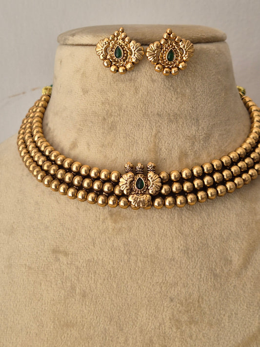 A gold-toned traditional jewelry set featuring a multi-strand beaded necklace with a decorative central clasp and matching stud earrings with green stone accents by naitri.in