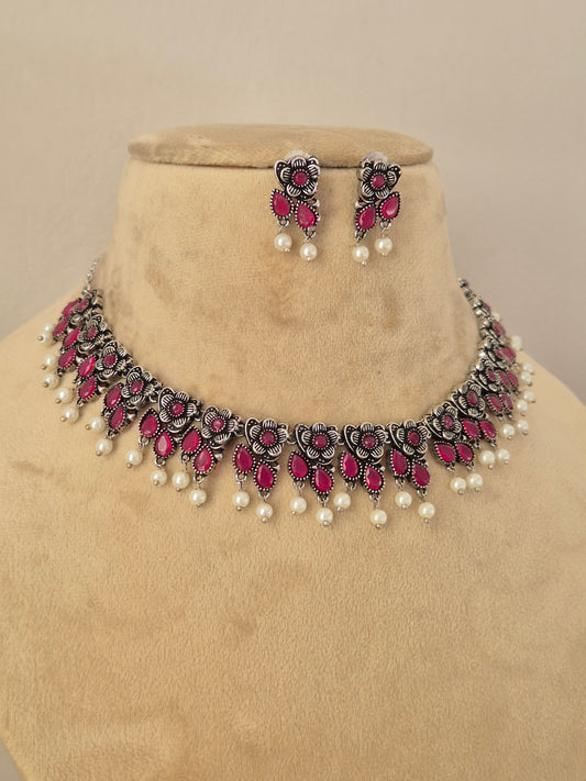 Pair of oxidized silver floral motif choker necklace with matching red stone earrings by Naitri.in
