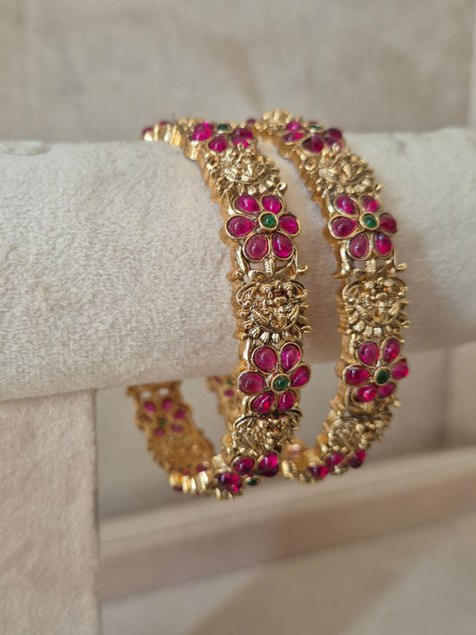 Close-up of Naitri Urmi premium gold ethnic bangle set with traditional Indian filigree engraving and vibrant red and green stone accents by naitri.in