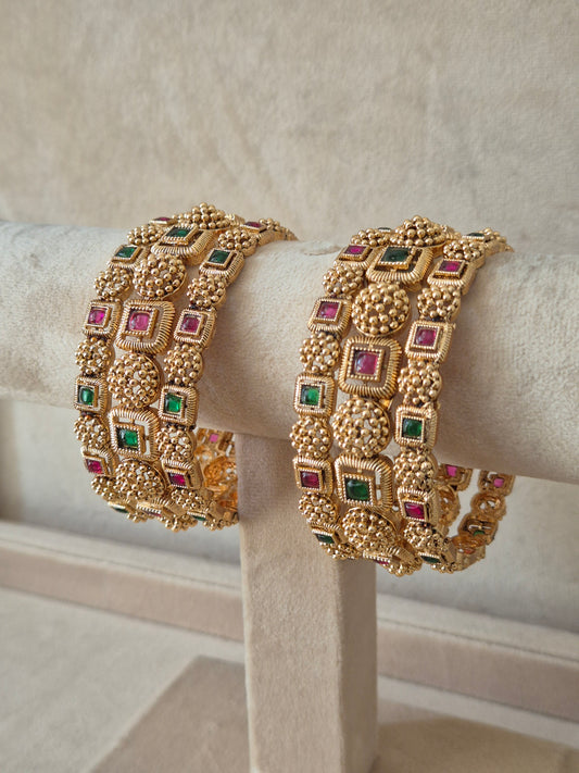 Close-up of Naitri Uttura premium gold ethnic bangle set with traditional Indian floral metalwork and vibrant red and green stone accents. by naitri.in