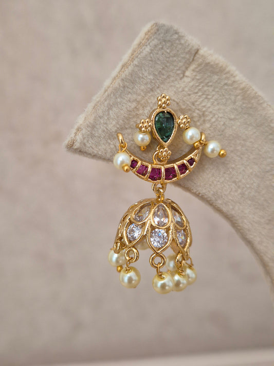 Traditional gold-polished brass Jhumka earrings with intricate floral metalwork, colorful stone embellishments, and dangling seed pearls for an ethnic Indian look by naitri.in