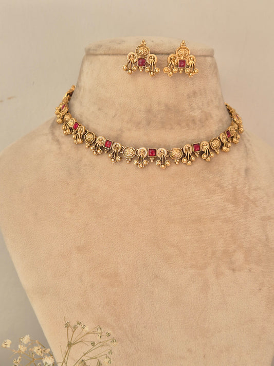 Gold-toned traditional Indian jewelry set featuring a choker necklace and matching earrings with red gemstone accents, by naitri.in