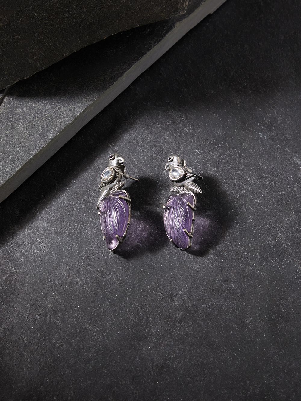 Purple stud earrings with stonework, displayed on a jewelry stand