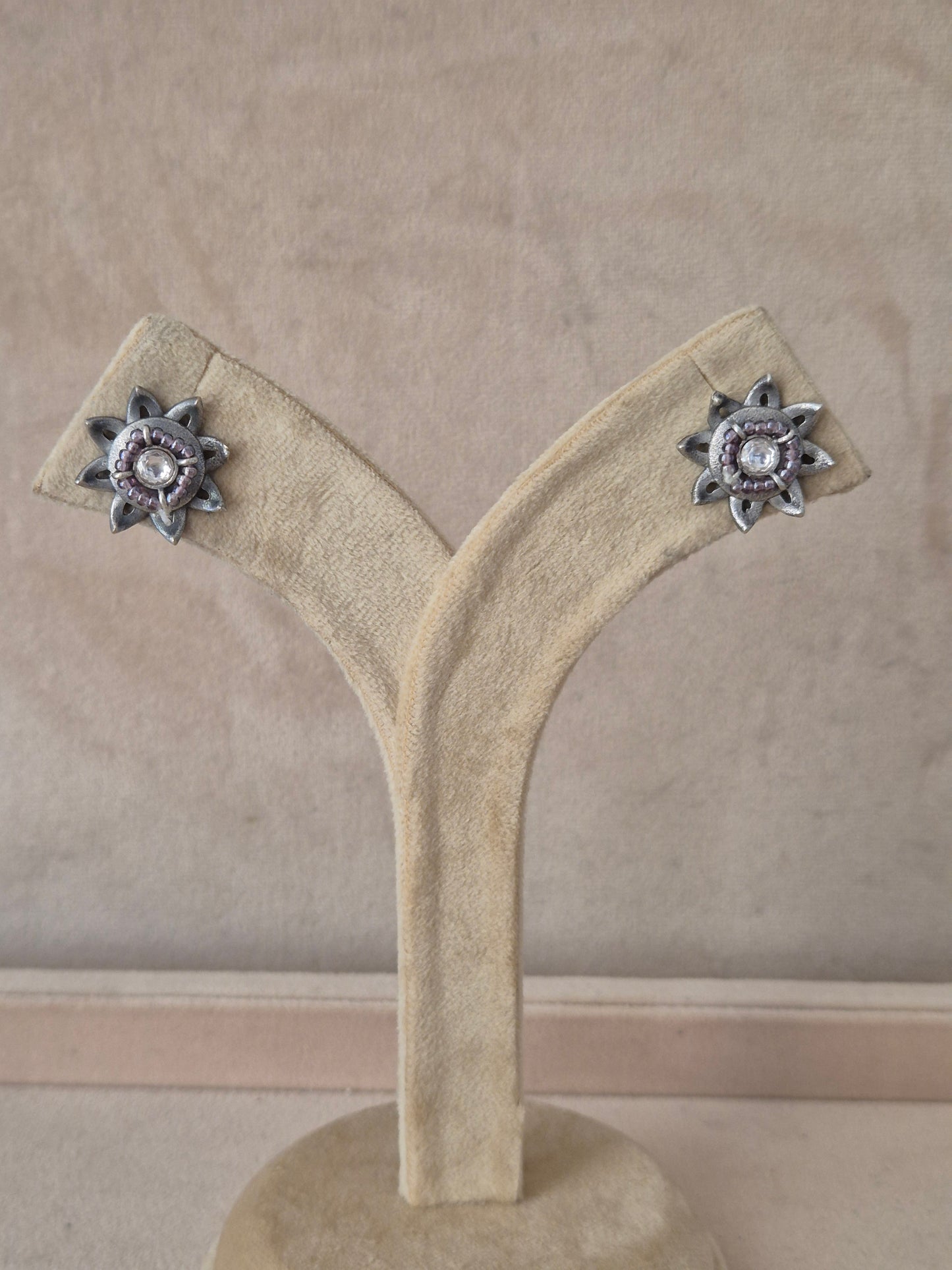Pair of Neerja silver-toned floral stud earrings featuring an intricate starburst design with a central white stone on a stand. Naitri premium Neerja oxidized silver stud earrings from the Silver Jewellery collection by naitri.in