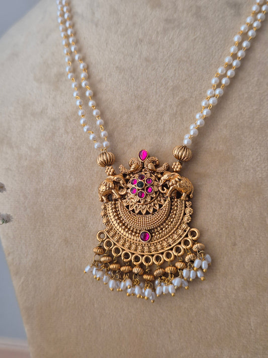Handcrafted brass alloy necklace set with a textured gold pendant, ruby-pink stone embellishments, and white pearl drops by naitri.in
