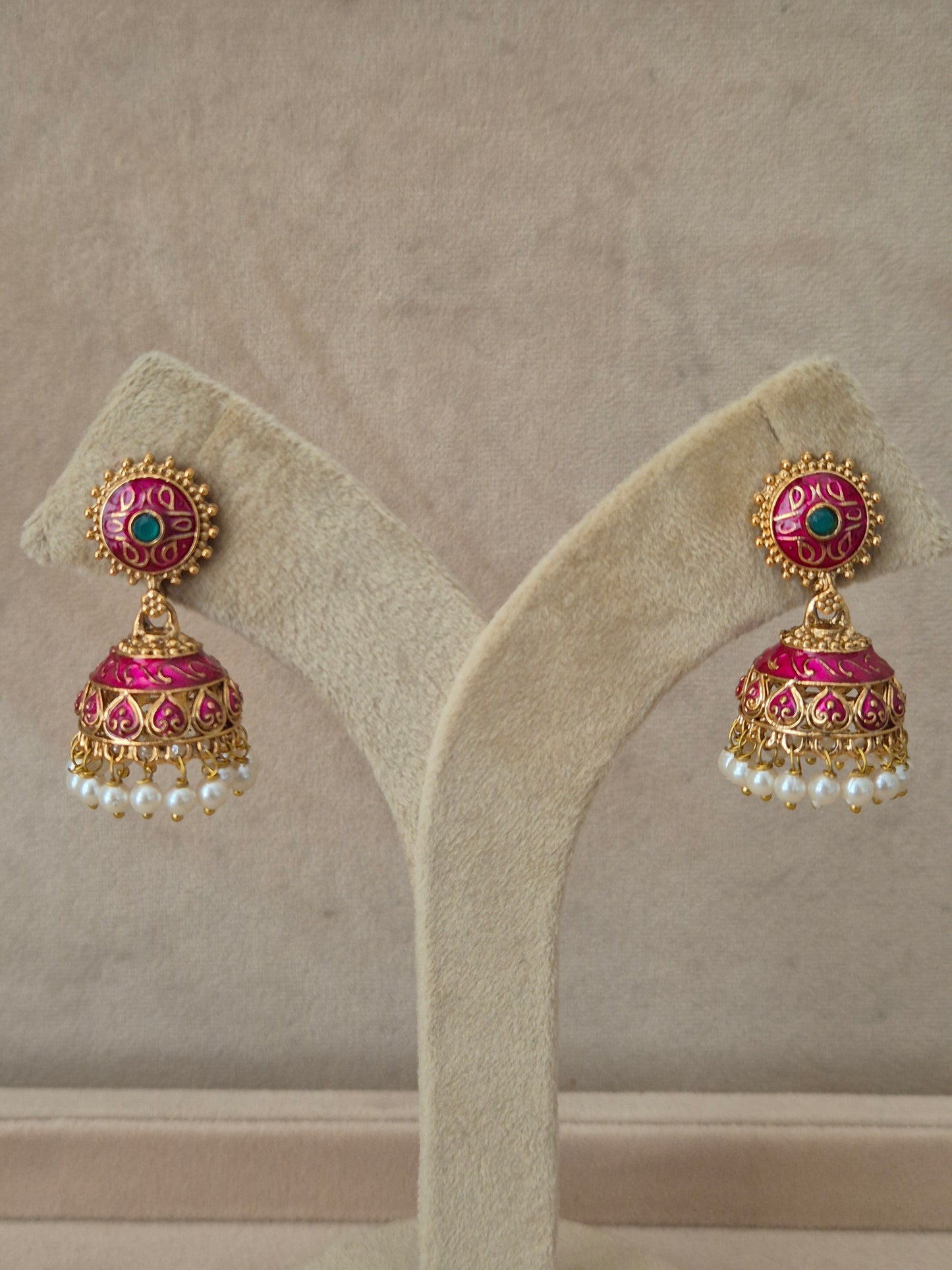 Close-up of Naitri Rakshita premium gold ethnic earrings showcasing traditional Indian Jhumka craftsmanship with intricate pink and green floral enamel accents and delicate pearl dangling beads. by naitri.in