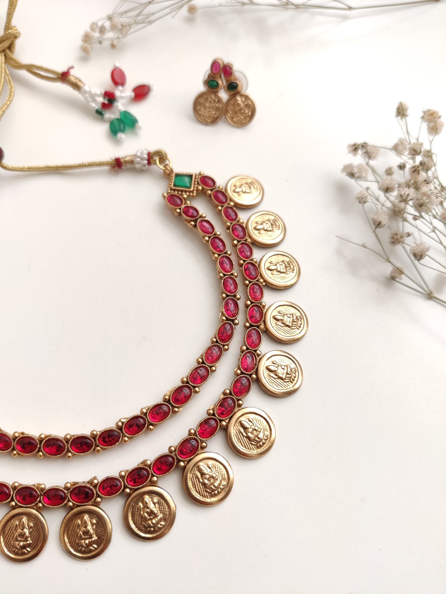 A necklace set with gold- adorned with red gemstones and coin-shaped embellishments by Naitri