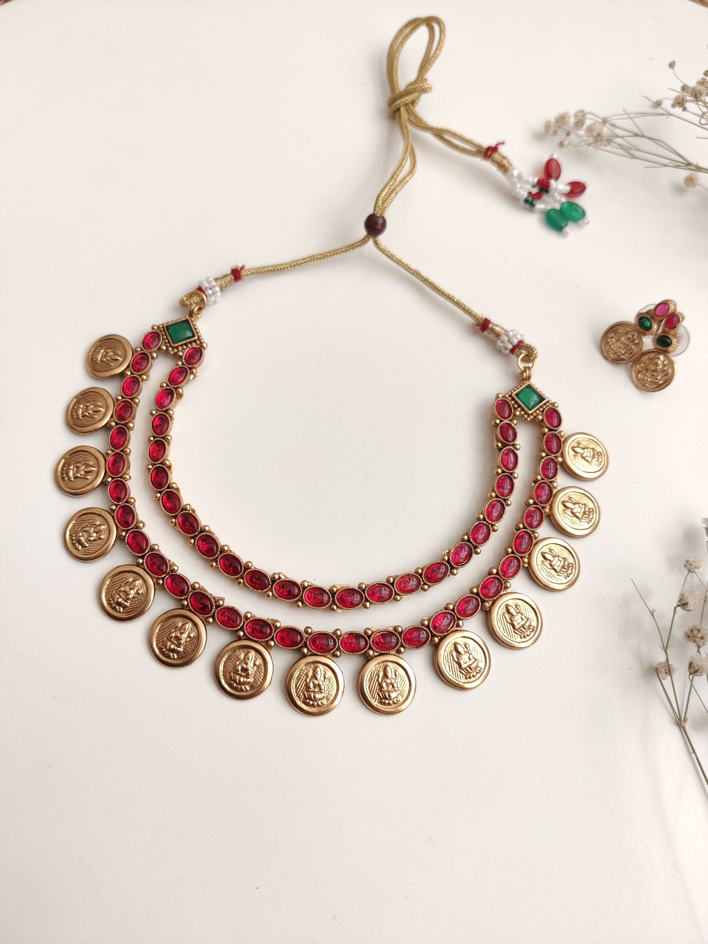 A necklace set with gold- adorned with red gemstones and coin-shaped embellishments by Naitri