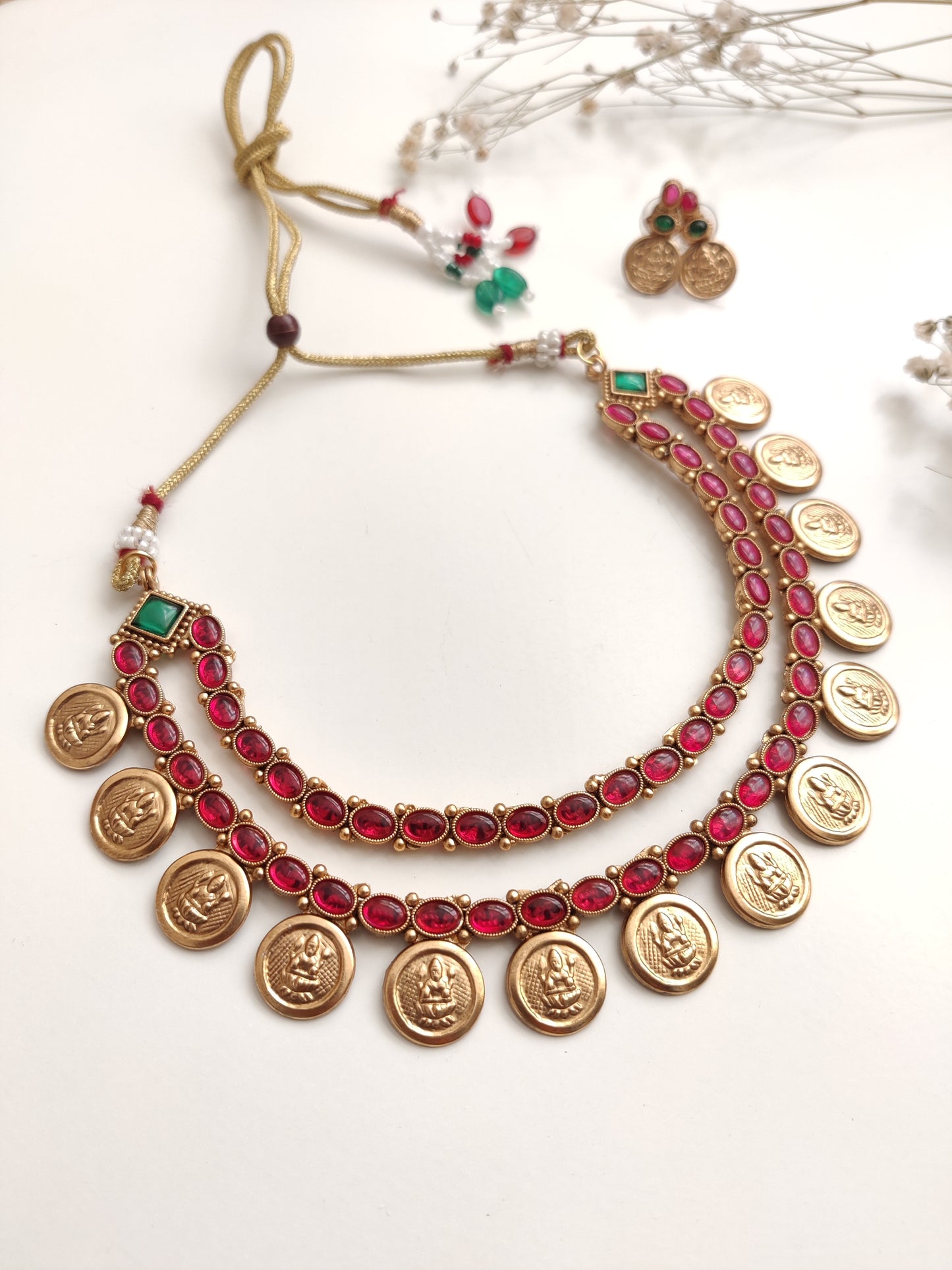 A necklace set with gold- adorned with red gemstones and coin-shaped embellishments by Naitri