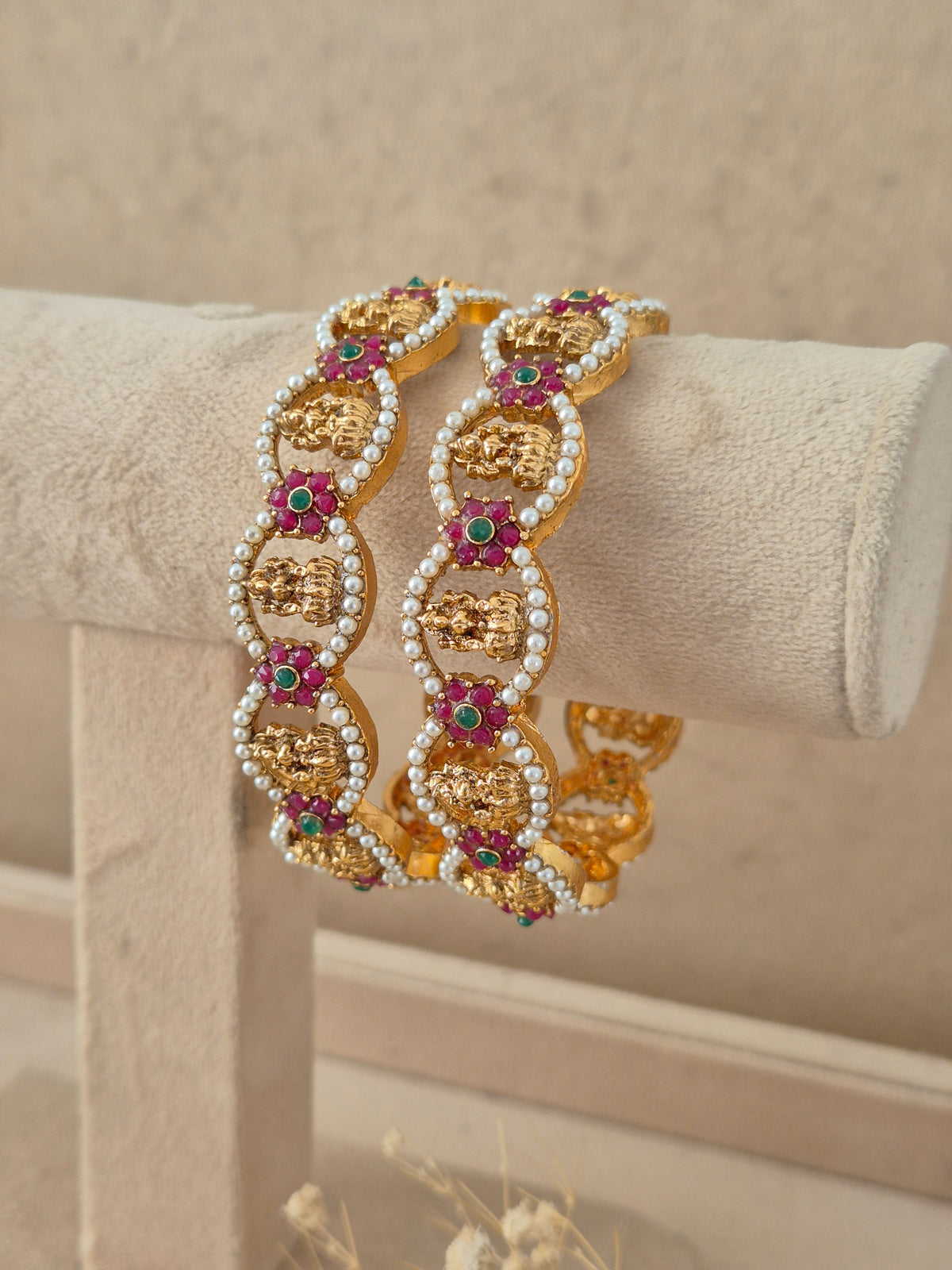 Royal Indian gold-plated bangles embellished with vibrant red and green stones and pearl borders for festive and bridal wear by naitri.in