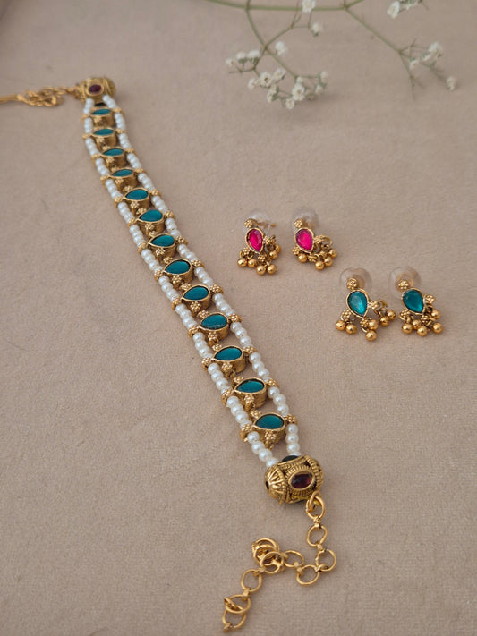 Handcrafted gold-plated brass choker featuring 2 rows of white pearls and vibrant blue stone in drop shaped in the middle of pearls row , paired with matching floral-themed earrings by naitri.in