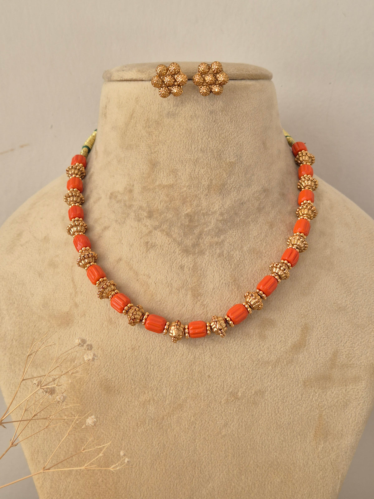 Close-up product view of a gold and orange bead necklace paired with small matching stud earrings