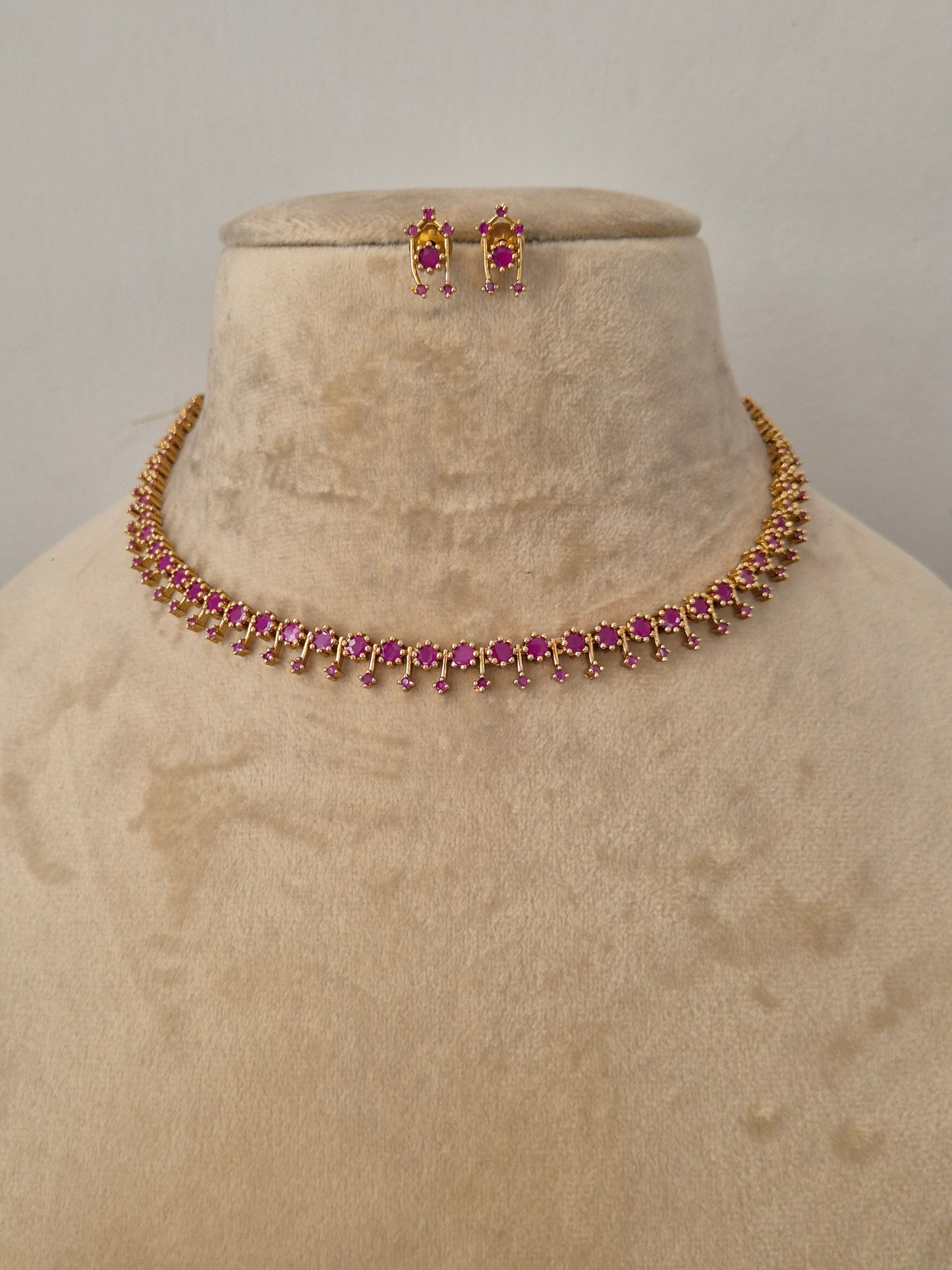 Gold-toned choker necklace and matching stud earrings with ruby-red stone embellishments by naitri.in