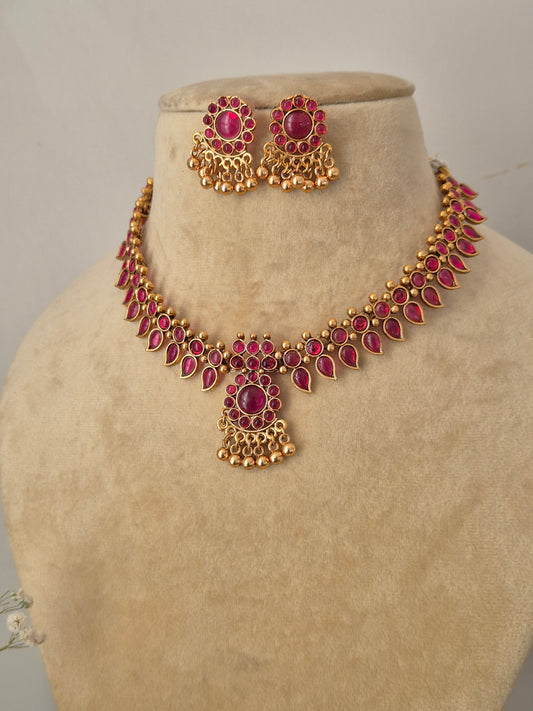 Traditional Indian-style gold-tone brass necklace featuring a central ruby pendant and a row of dangling red stone charms with matching round earrings by naitri.in