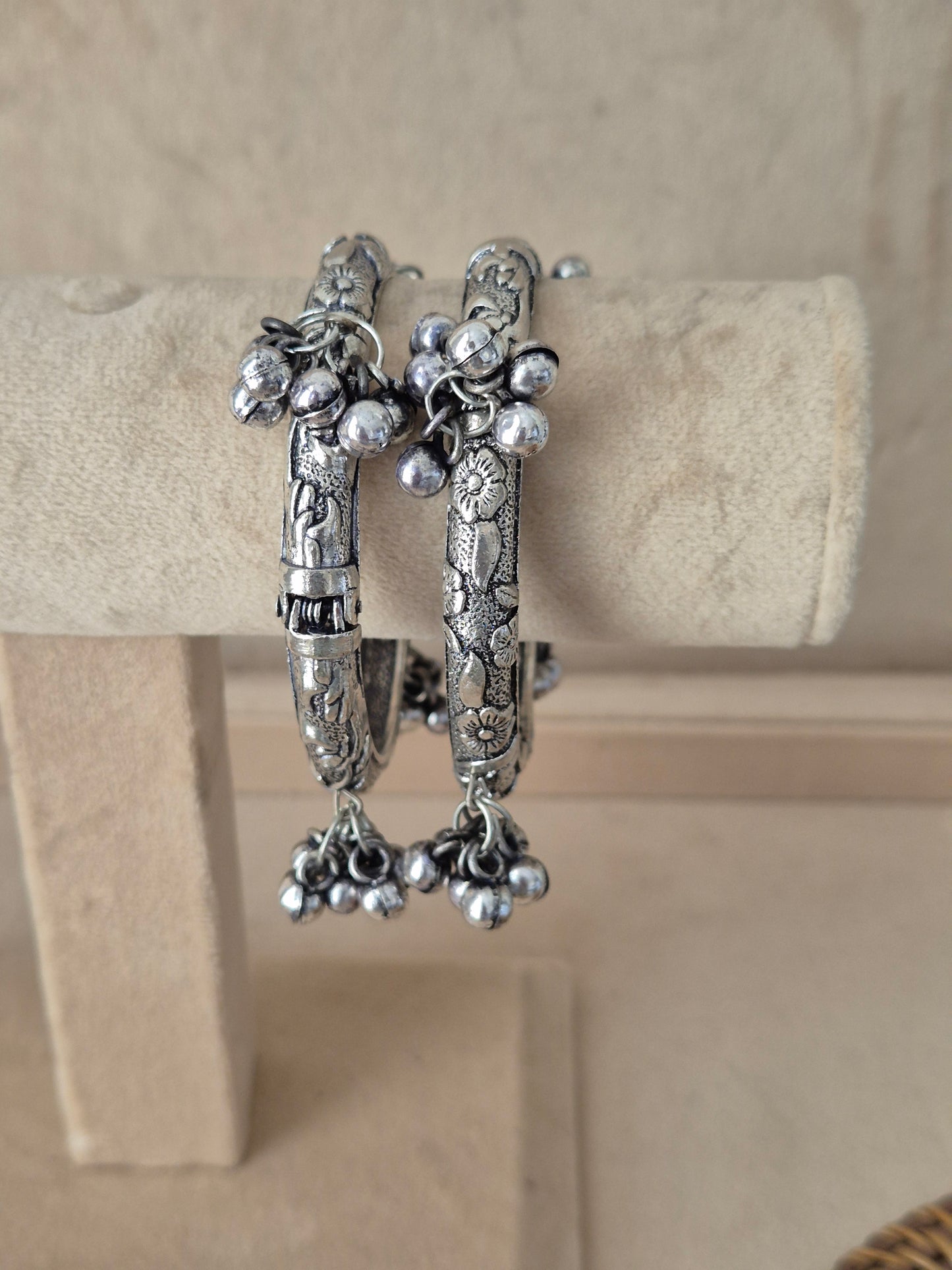 Set of 2 oxidized silver Wishi bangles with floral engravings and dangling jhumka charms. Elegant antique silver-toned tribal cuff bracelets with traditional festive details, by naitri.in