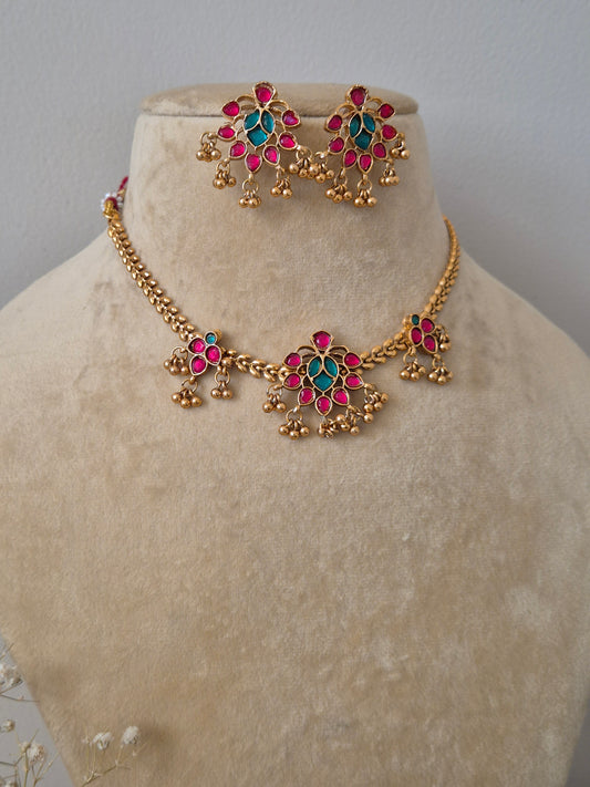 Handcrafted jewelry set in brass alloy with a polished golden finish, featuring traditional floral motifs and vibrant pink and green stones by naitri.in