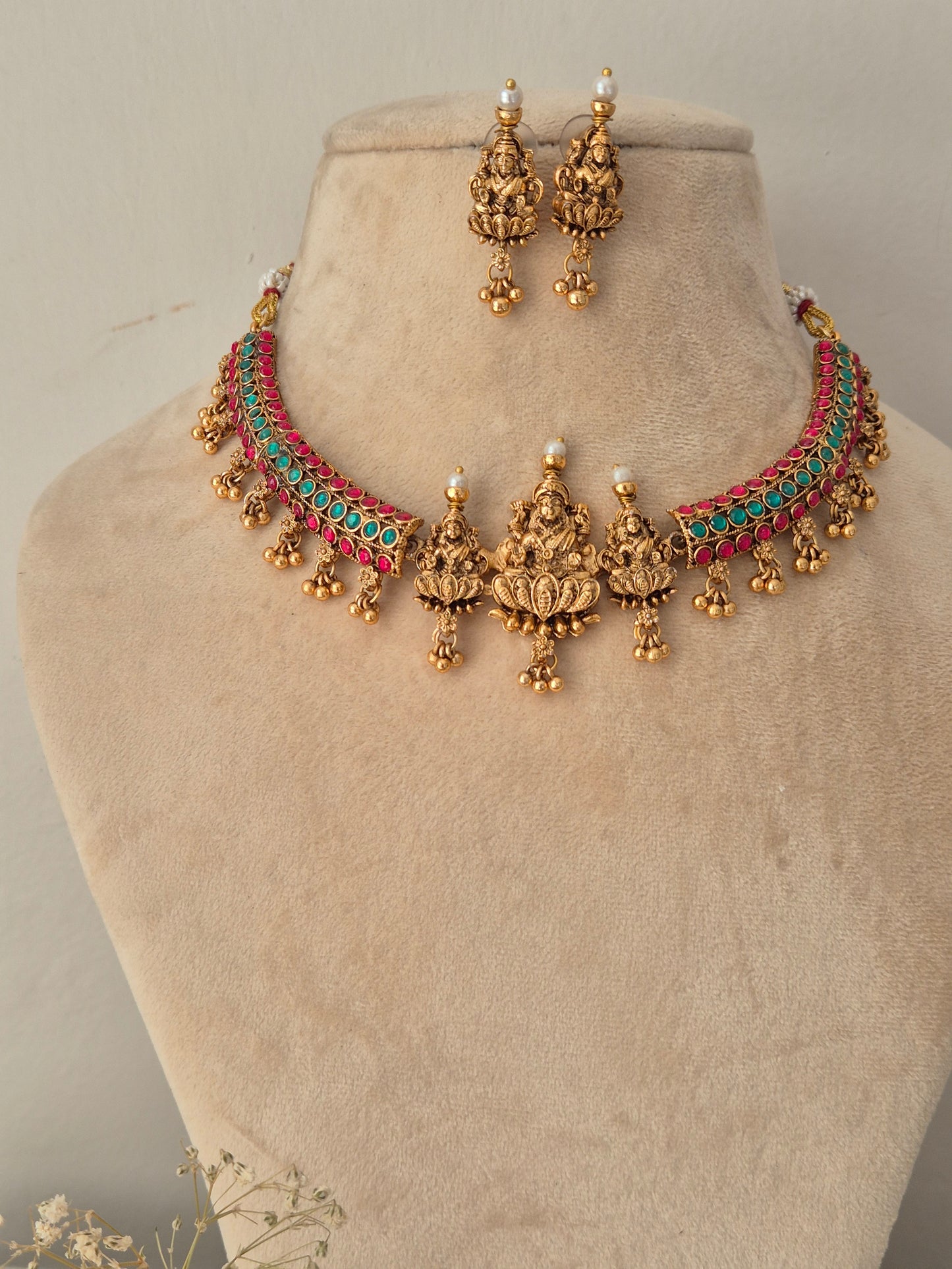 Gold-toned traditional Indian jewelry set including a choker necklace and matching earrings, decorated with red and green stones and gold bell details, by naitri.in
