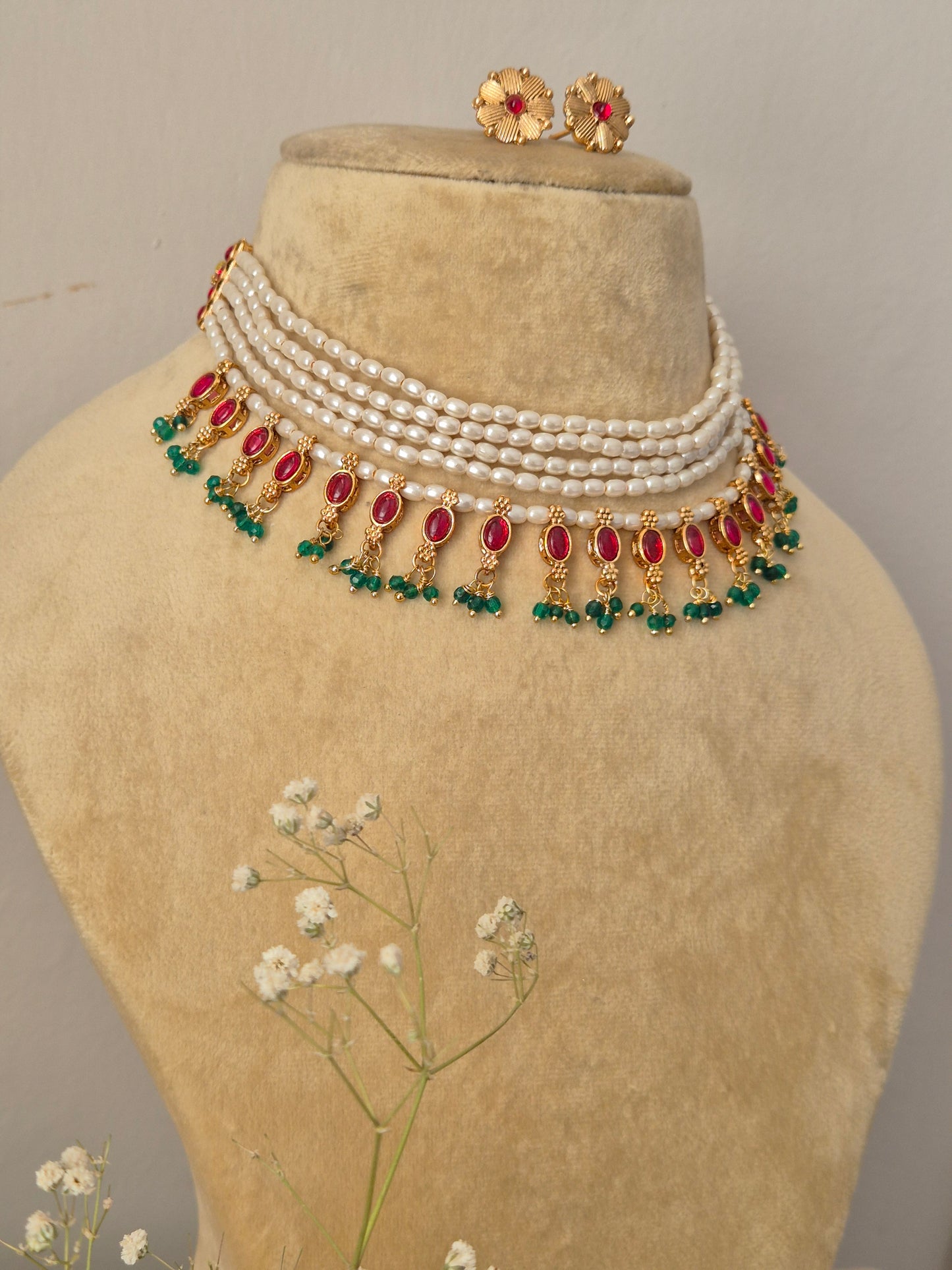 Artisanal Rashmi pearl necklace and earring set styled on a neutral cream display bust with a delicate sprig of white baby's breath flowers