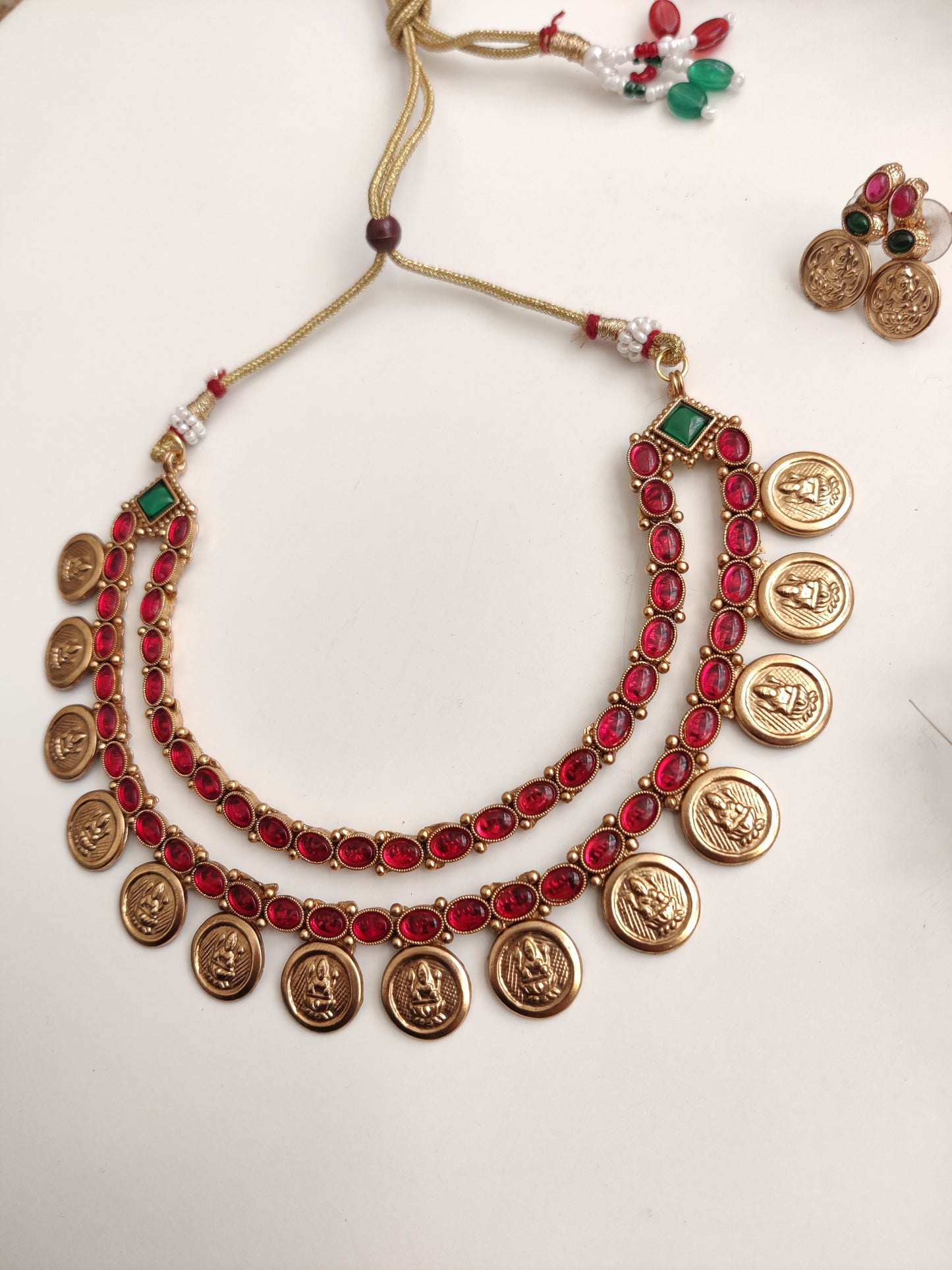 A necklace set with gold- adorned with red gemstones and coin-shaped embellishments by Naitri