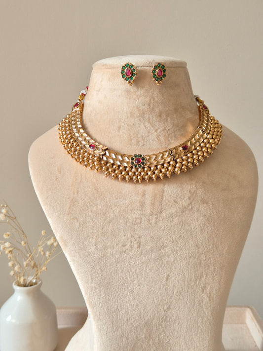 Statement gold necklace set with red accents, Trishani by Naitri, displayed flat.