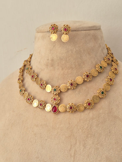 Yamya gold-toned double-layer coin necklace with red and green stones, styled with matching floral coin earrings on a mannequin bust.