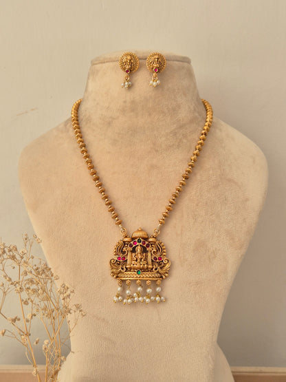 Yamira gold-toned temple necklace set with Goddess Laxmi pendant, red and green stones, pearl drops, and matching stud earrings.