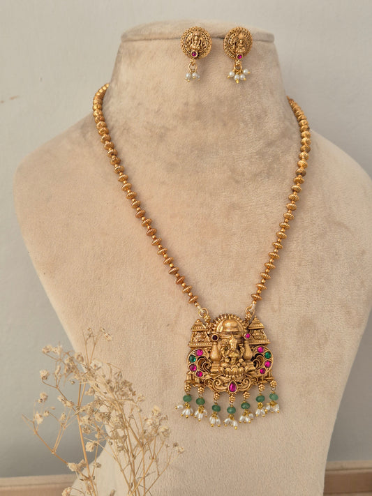 Traditional Indian gold-toned beaded chain necklace featuring an intricate temple pendant with a Goddess Laxmi motif, embellished with red and green stones and hanging white pearl drops, styled with matching round stud earrings