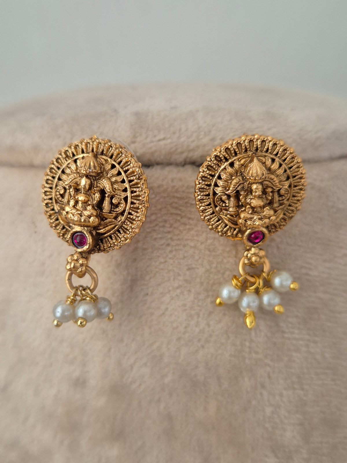 Circular gold-toned temple stud earrings featuring Goddess Laxmi motif, red stone center, and dangling pearl drops from the Yatishri set