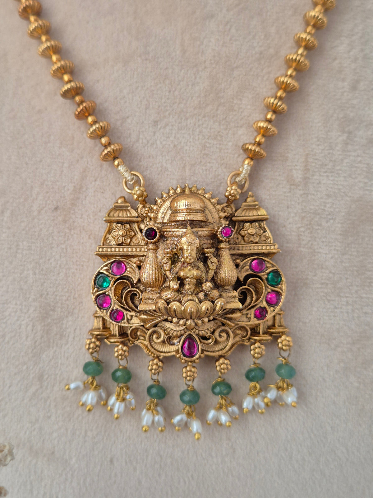 Close-up of Yatishri gold-toned temple necklace pendant featuring Goddess Laxmi, pink and green stones, and dangling pearl drops