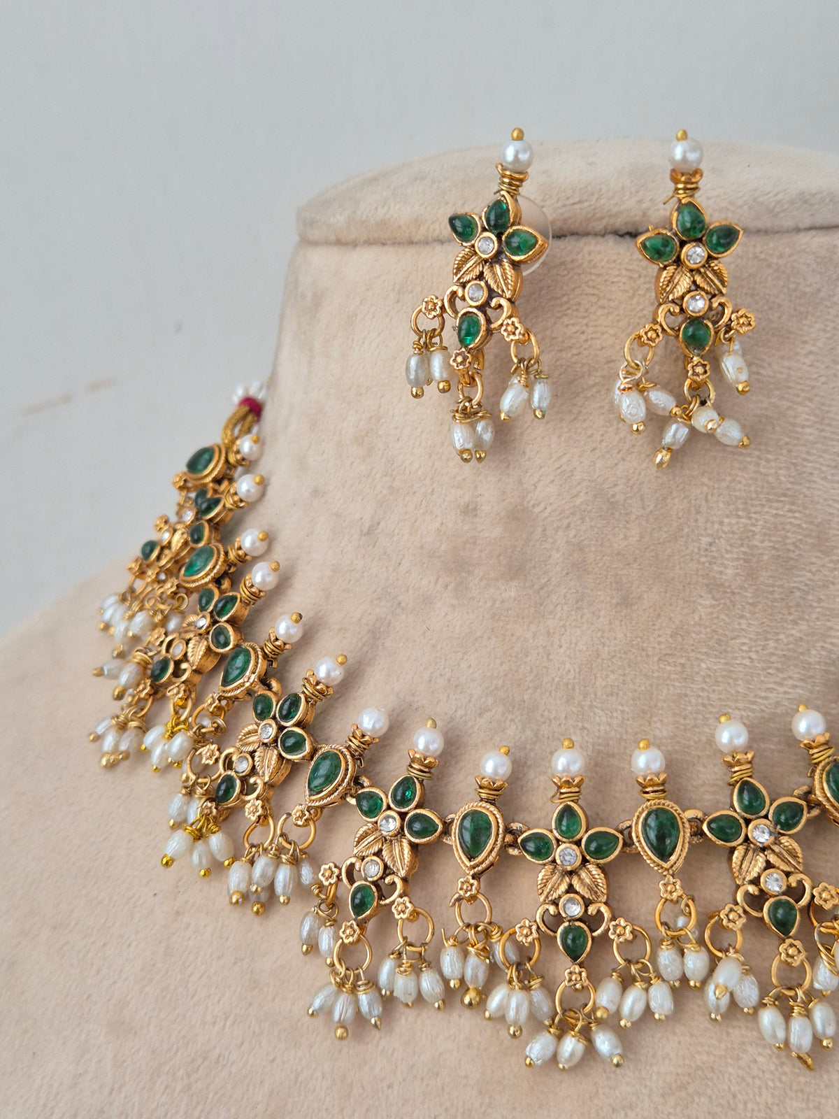 Close-up of Ladli gold-toned choker necklace with green floral stone motifs and hanging pearl clusters, paired with matching drop earrings
