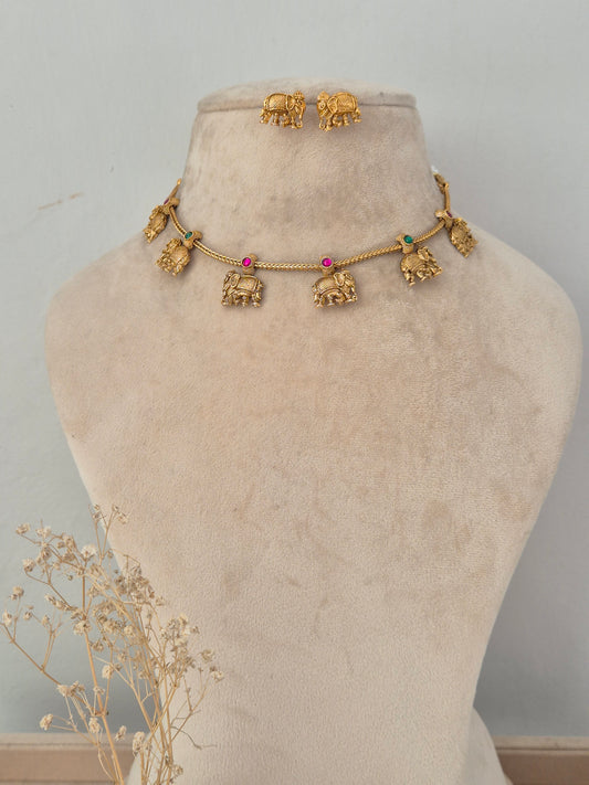 Upama gold-toned necklace set with elephant motif charms, red and green stone accents, and matching stud earrings