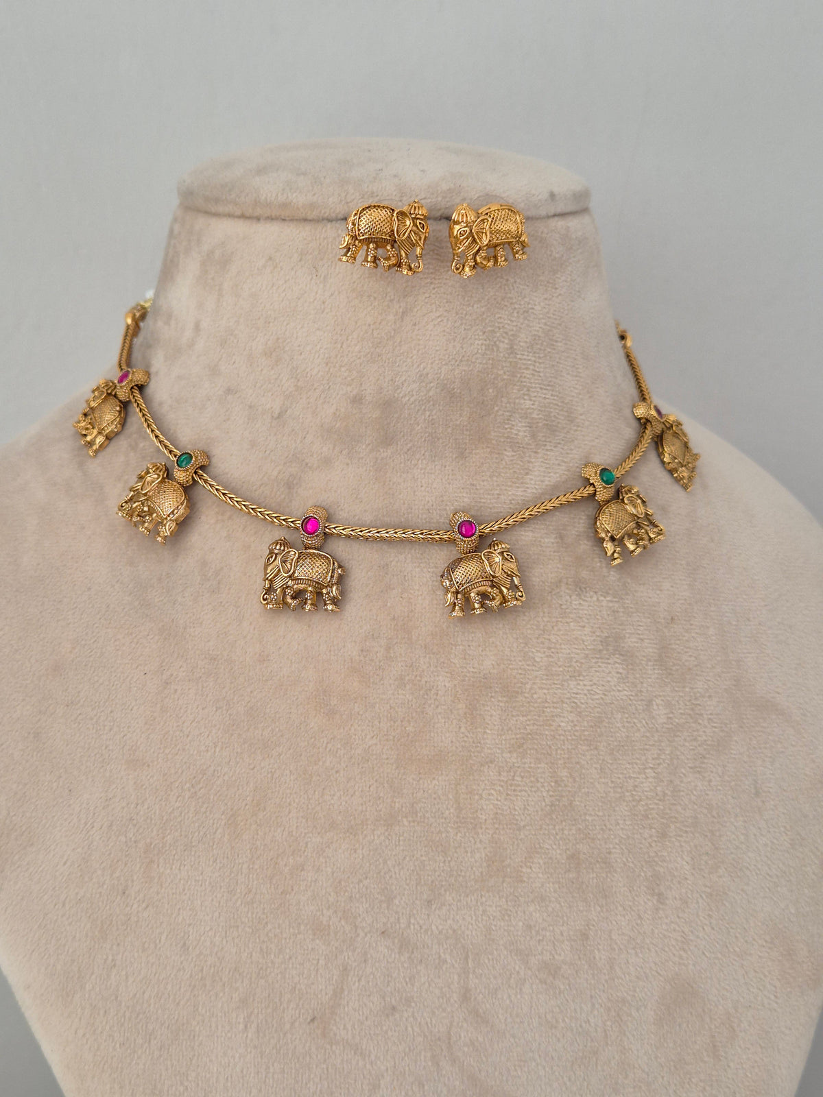 Upama gold-finish choker-style necklace with dangling elephant motifs and matching stud earrings on a beige bust
