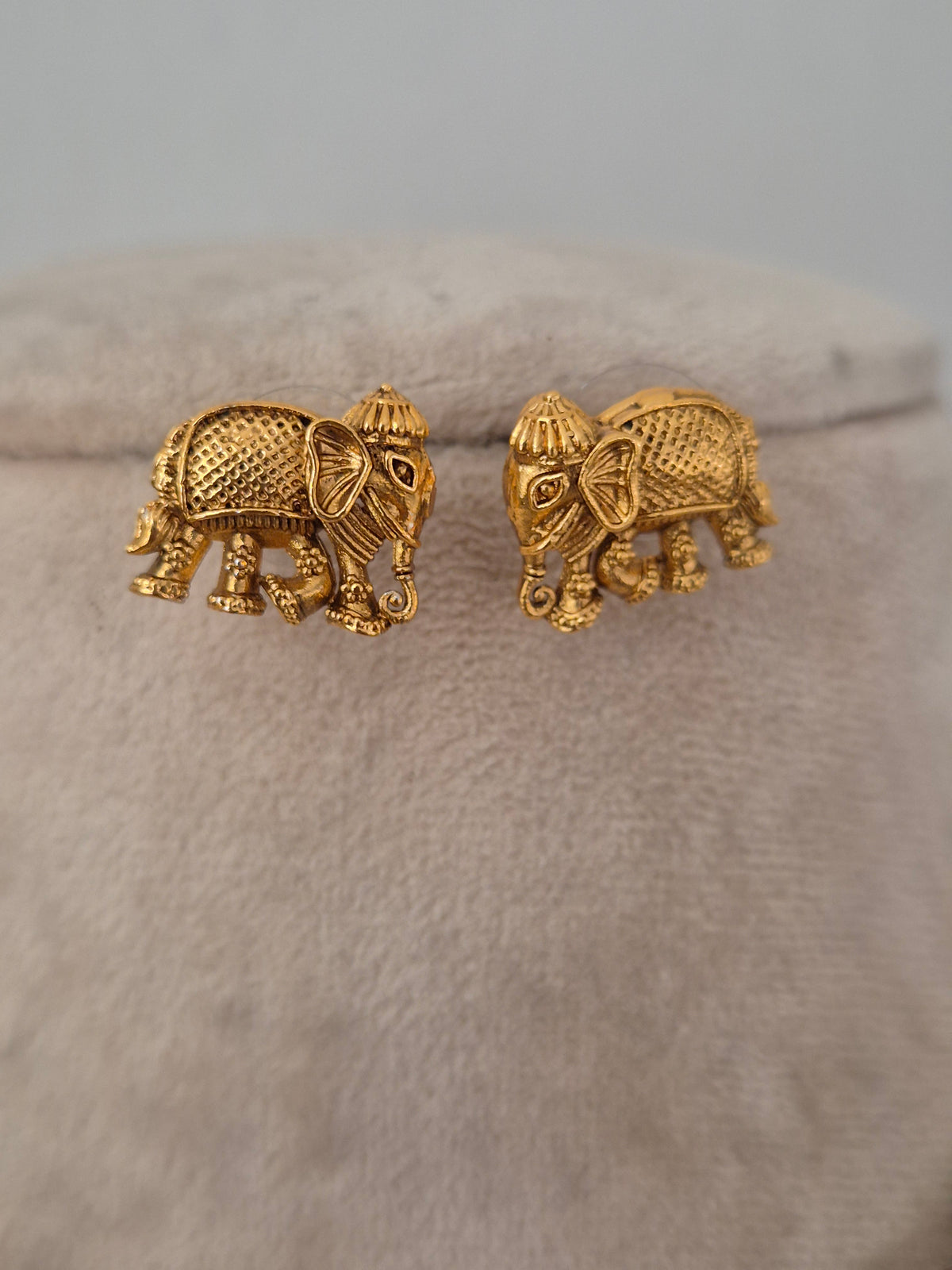 Close-up of Upama gold-toned necklace featuring hanging textured elephant charms with red and green stone accents