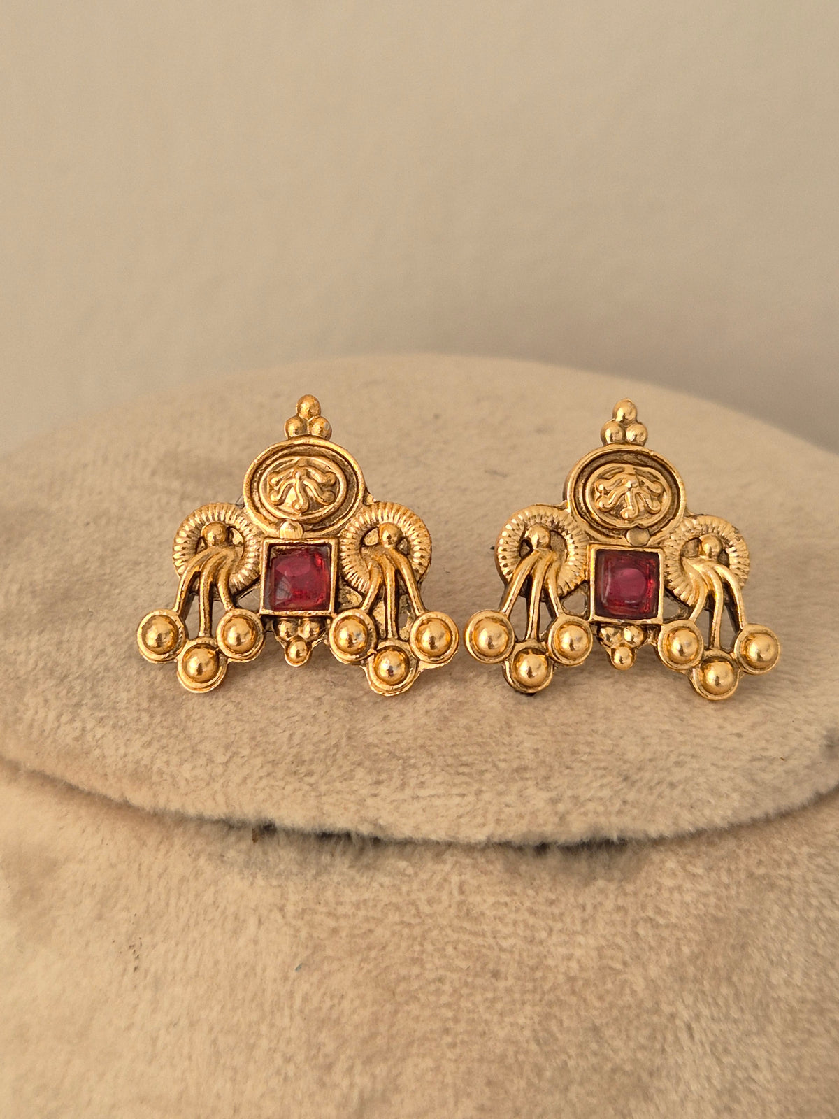 Matching gold-finish brass alloy stud earrings featuring square red stone centers and intricate traditional bead accents