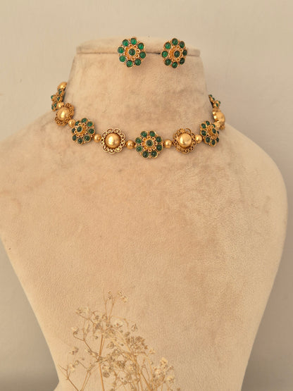 Traditional gold-toned choker necklace featuring alternating textured gold domes and floral motifs embellished with green stones, paired with matching floral stud earrings