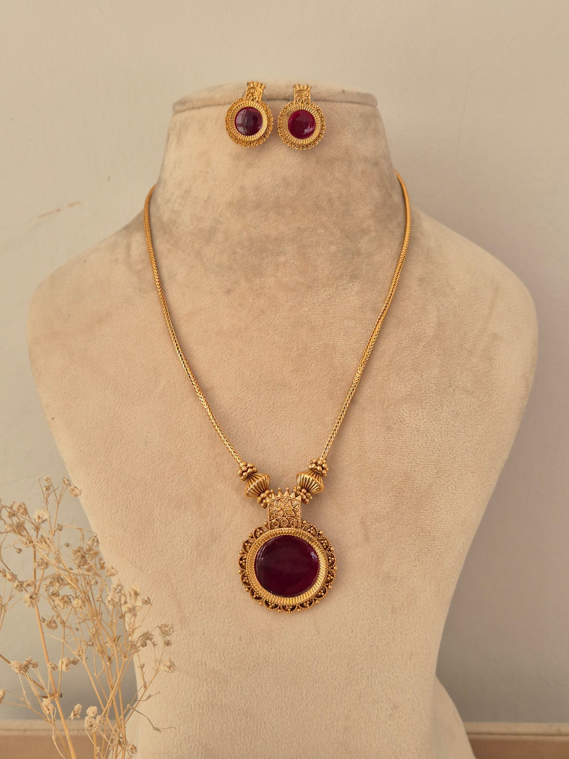 Antique gold-toned Yogisha chain necklace set featuring a round deep red gemstone pendant with ornate border details