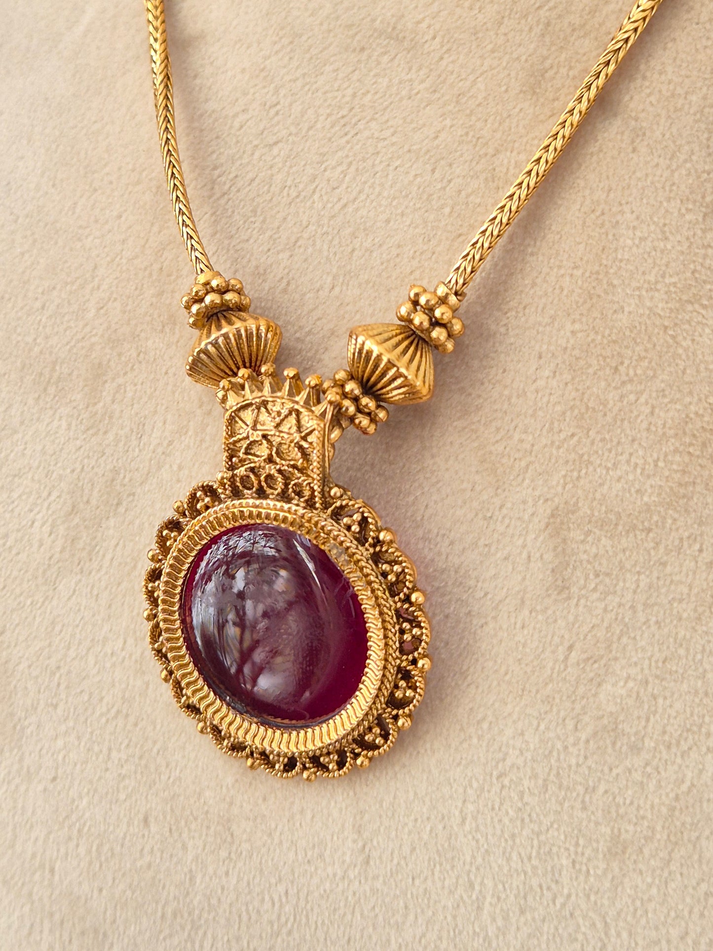 Antique gold-toned pendant necklace with a large round deep red oval cabochon stone in an ornate filigree setting