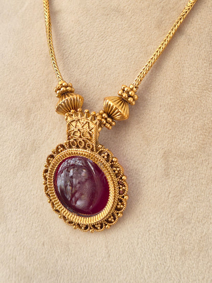 Antique gold-toned pendant necklace with a large round deep red oval cabochon stone in an ornate filigree setting
