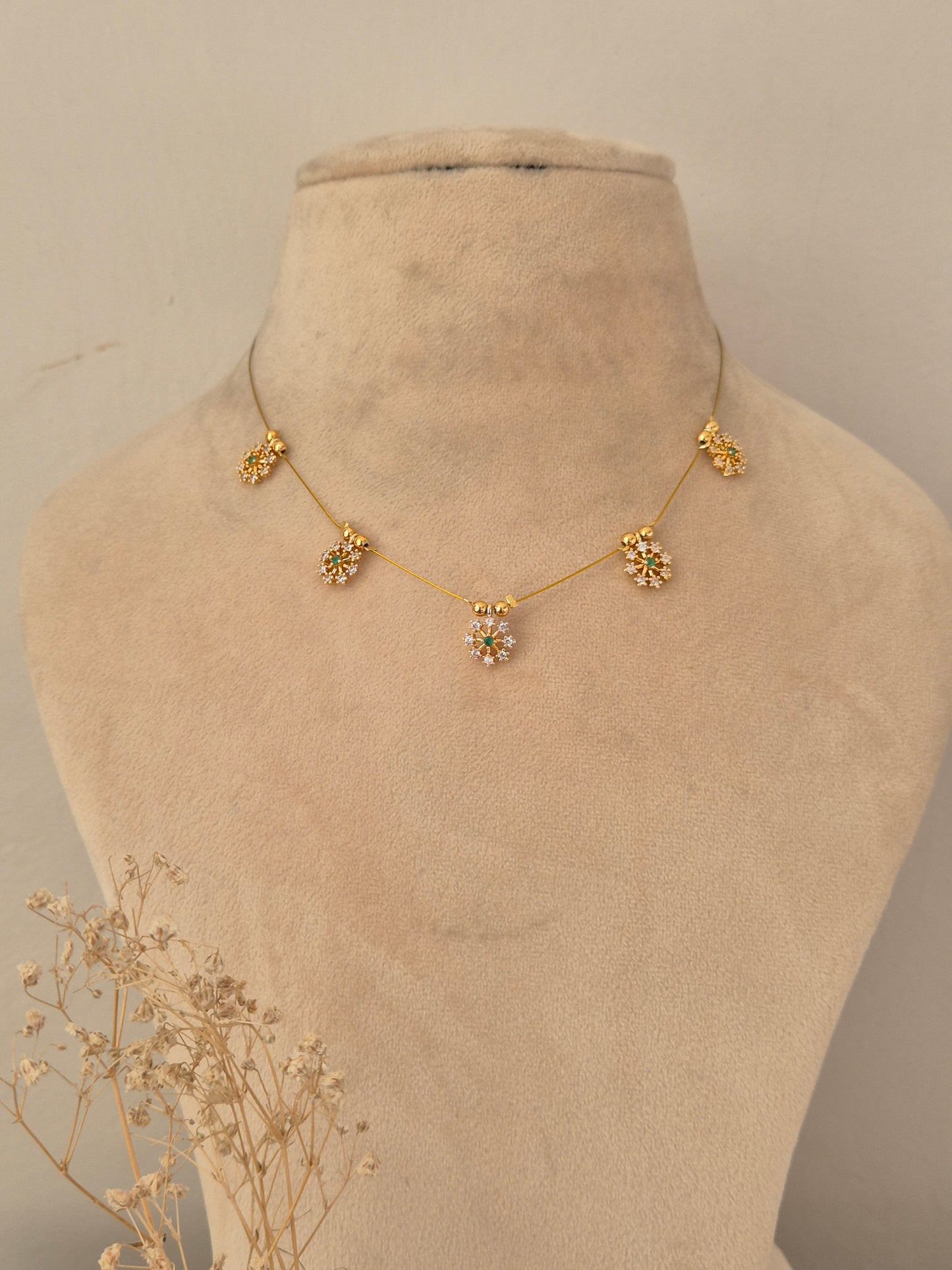 Descriptive & SEO-focused: Gold-finish invisible chain necklace featuring five floral stone-studded motifs with subtle green accents
