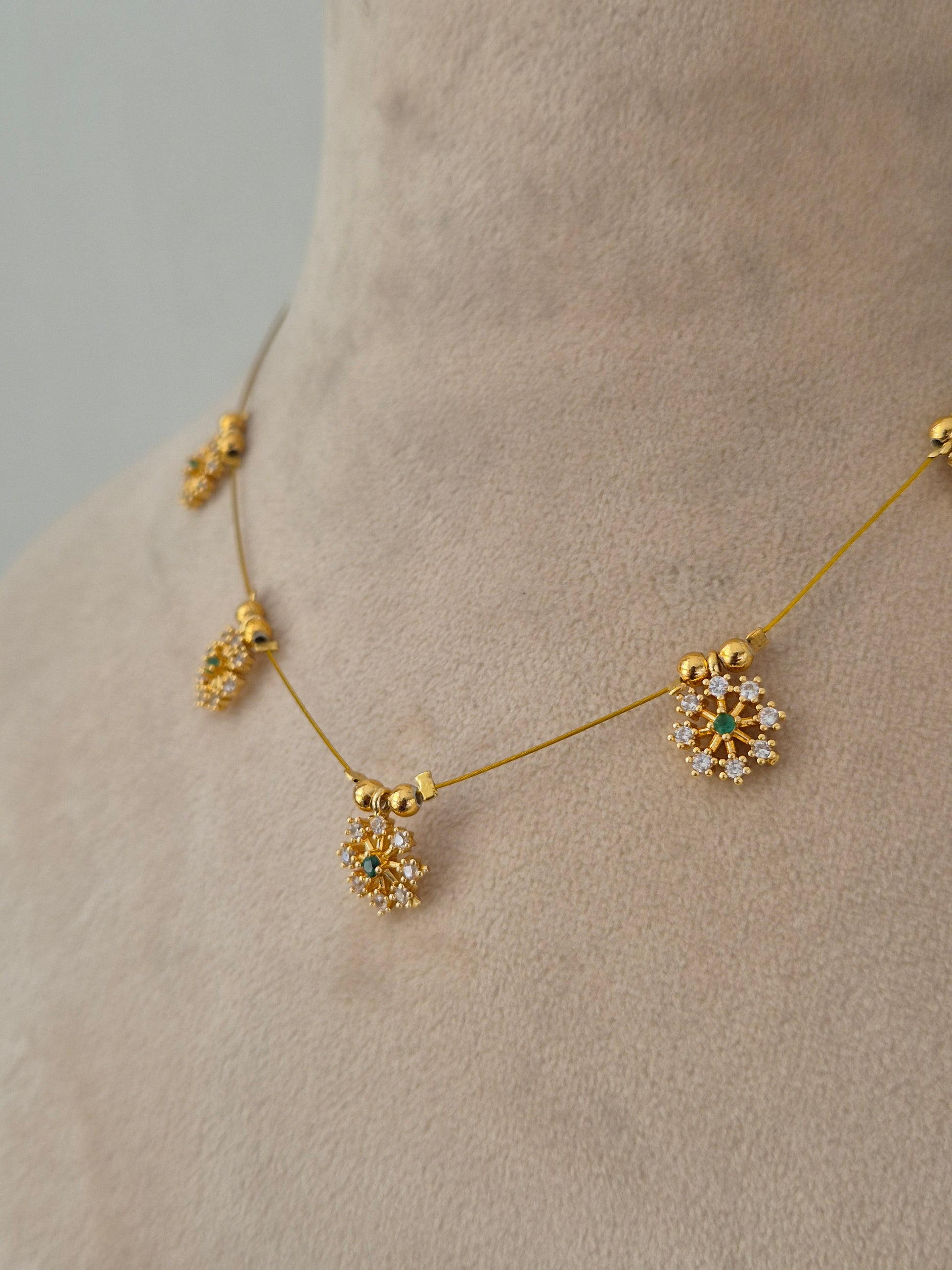 Delicate gold-toned necklace designed with a minimal transparent wire appearance, holding five sparkling floral starburst charms set with clear and green stones