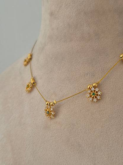 Delicate gold-toned necklace designed with a minimal transparent wire appearance, holding five sparkling floral starburst charms set with clear and green stones