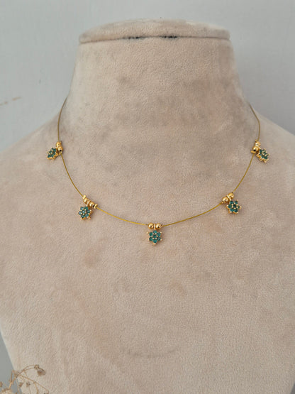 Delicate, transparent-style gold wire necklace holding five starburst floral charms centered with green stones
