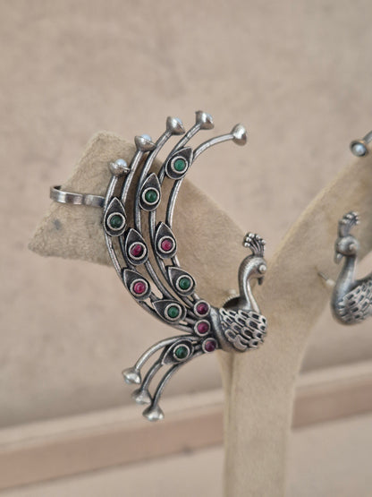 Pair of silver-toned peacock-shaped ear cuffs set with small circular pink and green stone inlay along the feathers