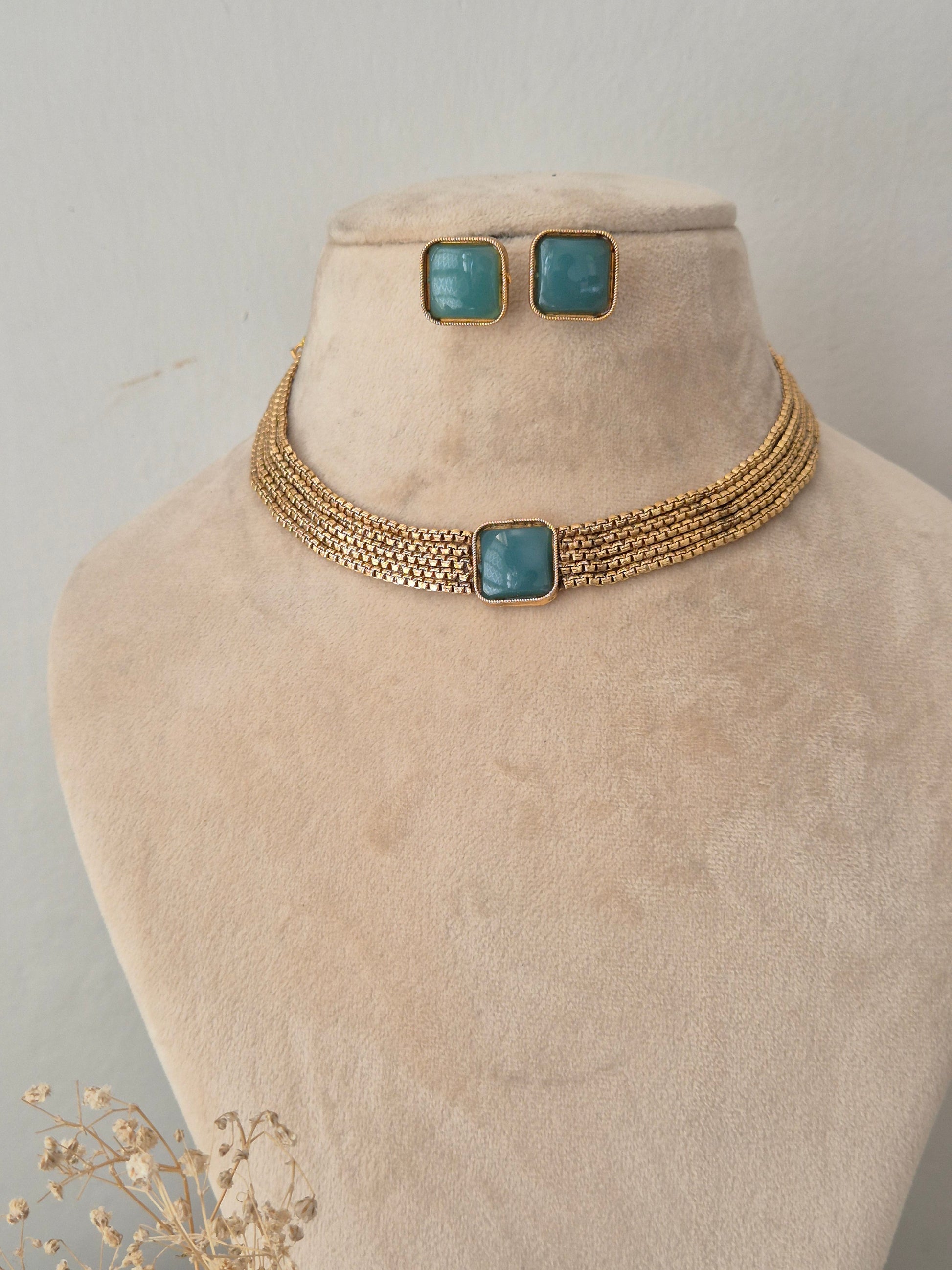 Multi-strand woven gold collar necklace with a central square teal stone and matching stud earrings