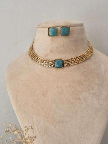 Multi-strand woven gold collar necklace with a central square teal stone and matching stud earrings