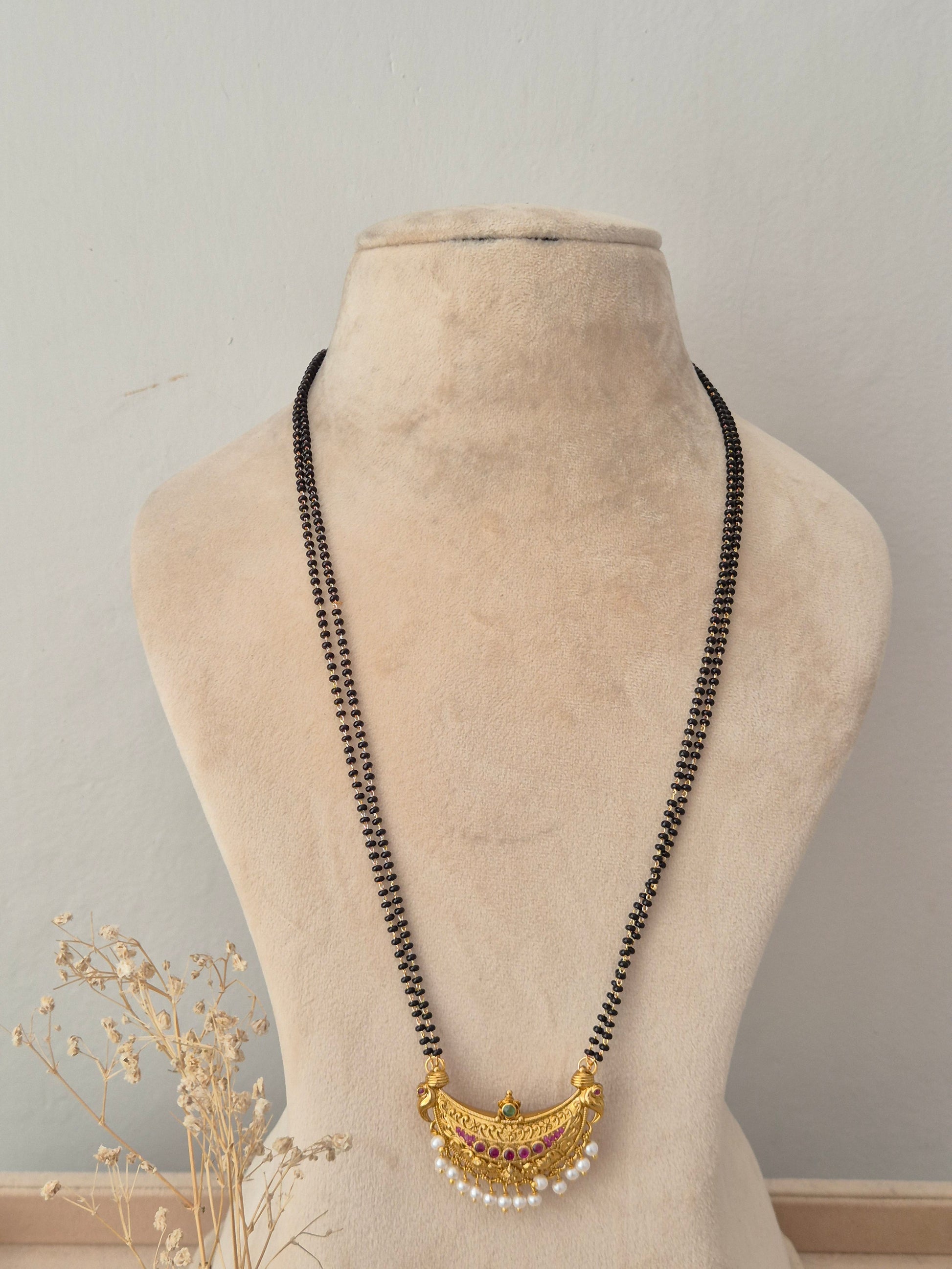 Elegant multi-strand black bead necklace with an artisanal gold crescent motif and dangling pearl accents