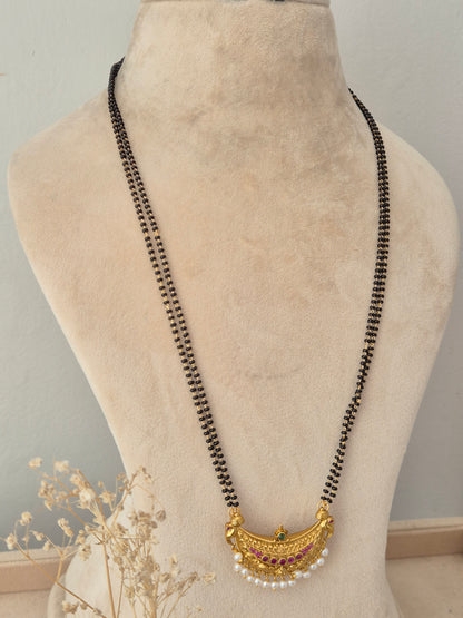 Prakriti Mangalsutra – Long multi-strand black bead chain with a gold crescent-shaped pendant embellished with pink gemstones, a green center stone, and dangling white pearl drops