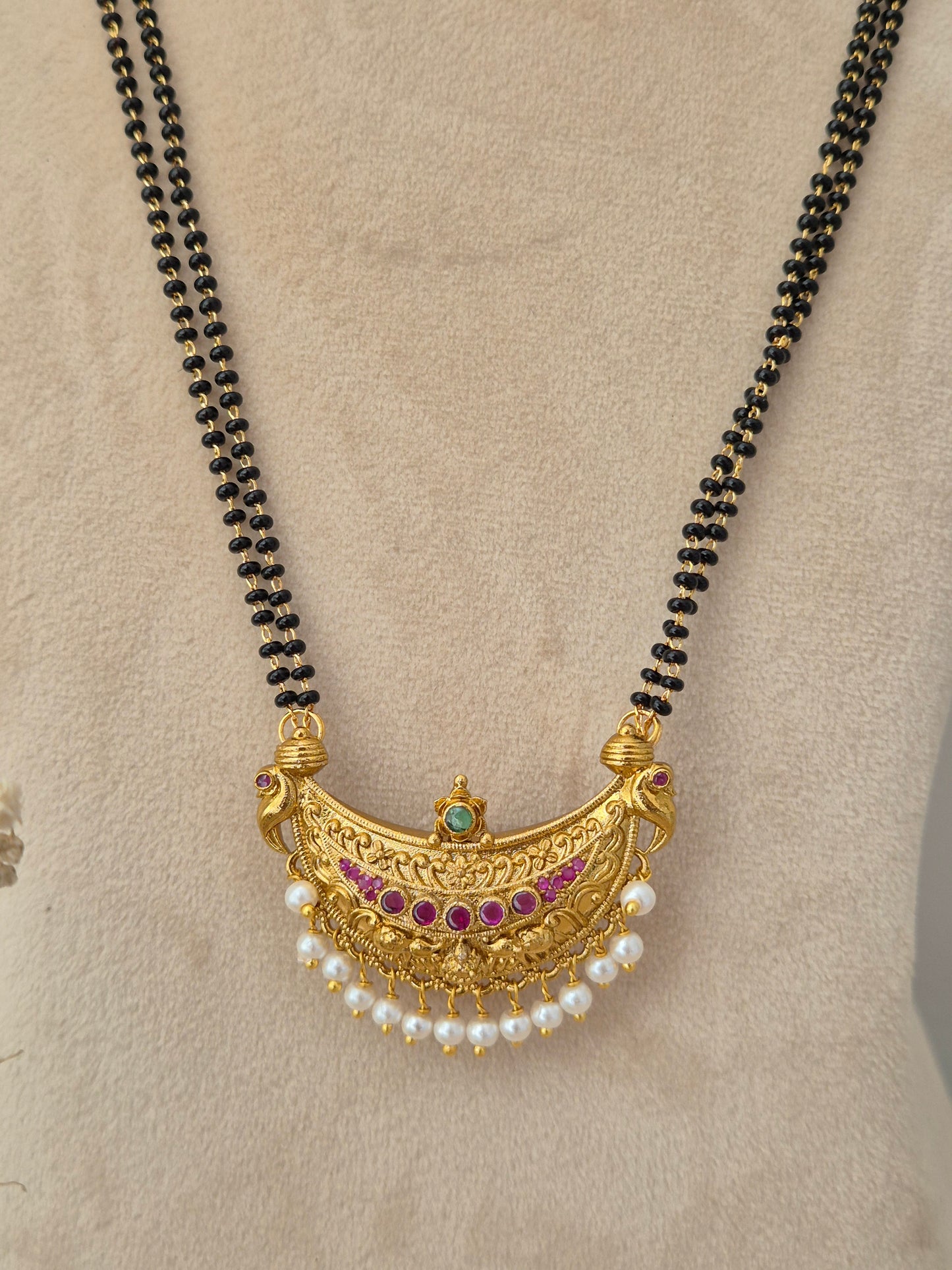 Multi-strand black bead chain with an intricate gold crescent pendant featuring pink gemstones, a green center stone, and dangling white pearl drops