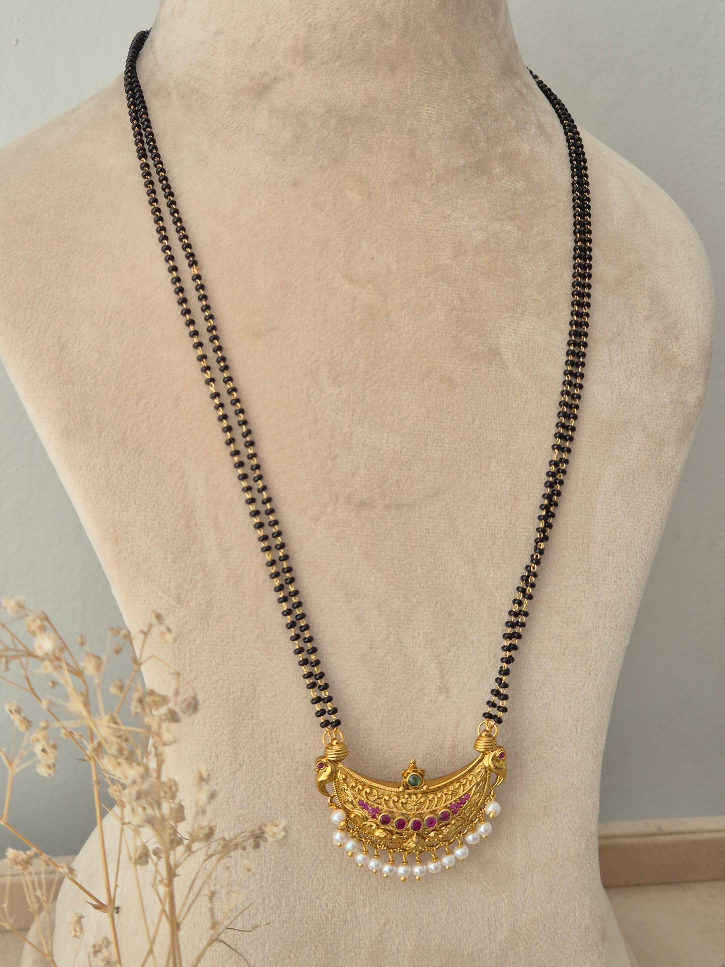 Traditional Indian black beaded mangalsutra chain featuring a gold crescent pendant accented with ruby pink and emerald green stones and pearl droplets